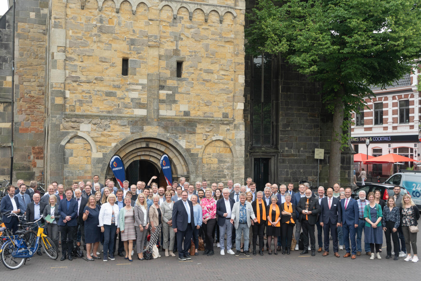 Ein Gruppenfoto von allen anwesenden Teilnehmer:innen. Sie stehen auf dem Oude Markt in Enschede vor der Oude Kerk.